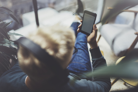 Young man wearing casual clothes sitting on comfort sofa and using smartphone at modern place.Horizontal.Blurred backgroundの写真素材