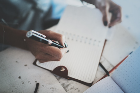 Beautiful young businesswoman writing something in note pad while sitting on armchair at living room.Charming female studying doing homework at home.Horizontal.Blurred backgroundの写真素材