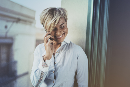 Portrait of smiling businesswoman talking with partner on smartphone device while working remotely in business travel.Attractive woman owner communicating on cellular while looking at camera.Blurred.の写真素材