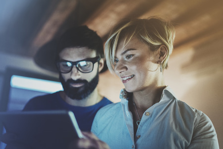 Happy family couple using electronic tablet in livingroom at home.Bearded man in eye glasses making conversation with young blonde woman at night. Blurred background.の写真素材