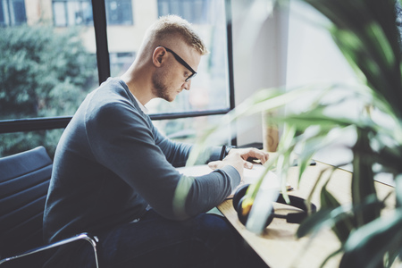 Skilled designer caucasian man drawing abstract sketch with pen.Art work process.Creative hobby.Noting ideas in copy book on workspace desk with papers in modern studio with panoramic windows.Blurred.の写真素材