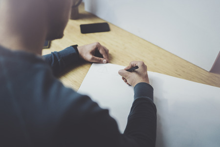 Skilled designer caucasian man drawing abstract sketch with pen.Art work process.Creative hobby.Noting ideas in copy book on workspace desk with papers in modern studio with panoramic windows.Closeup.の写真素材