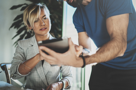 Coworkers working process at home.Young blonde woman working together with bearded colleague man at modern home office.People using electronic devices.Blurred background.Horizontal.の写真素材