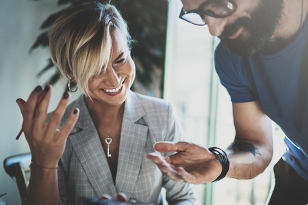 Coworkers working process at home.Young blonde woman working together with bearded colleague man at modern home office.People making conversation together.Blurred background.Horizontal.の写真素材