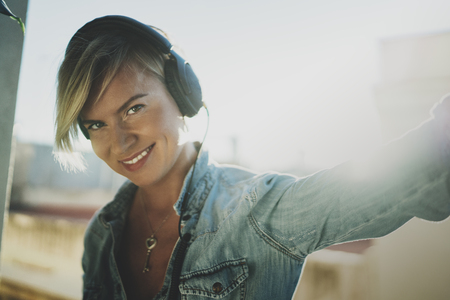 Smiling beautiful girl relaxing at home,wearing casual clothes,playing music,using smartphone and listening audio books in modern headphones.Young pretty woman music lover at room.Blurred background.の写真素材