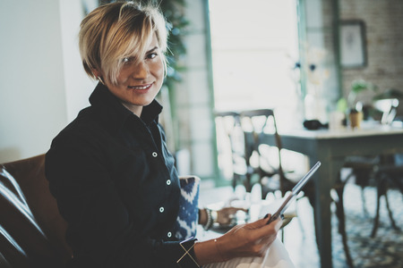 Smiling young woman wearing casual clothes and using electronic device while spending relax time home livingroom.Attractive woman owner communicating on digital tablet.Blurred background.の写真素材