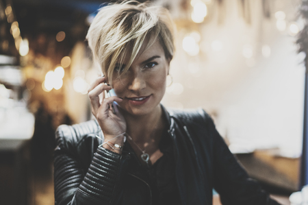 Young girl using smartphone on background glow bokeh light in night atmospheric city.Hipster girl using in hands and talking mobile phone.Blurred background.の写真素材