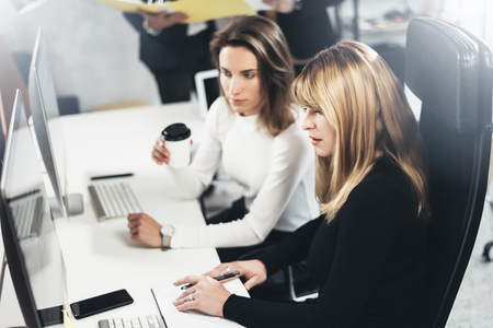 Two beautiful business woman making conversation at modern lightfil office.Handsome girls at working process.Horizontal,blurred background.の写真素材