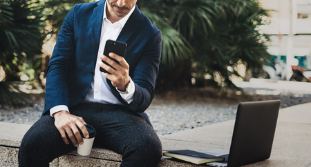 Attractive smiling businessman making video conversation with partners by mobile phone.Man using contemporary smartphone sitting outside.Blurred background. Horizontal. Cropped.の写真素材