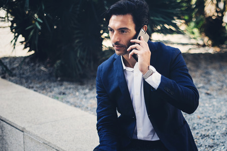 Elegant young businessman working outside with mobile laptop pro. Handsome man using modern smartphone for call.Blurred background.Horizontal.Cropped.の写真素材