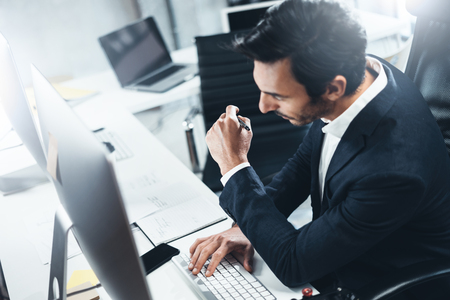 Confident man in formal wear thinking and working with desktop computer at modern lightful office.Horizontal.Blurred background.の写真素材