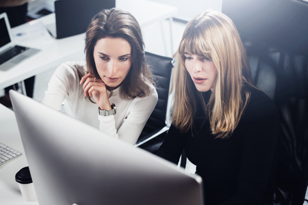 Two beautiful business woman working at modern lightfil office.Handsome girls at working process on desk top computer.Horizontal,blurred background.Cropped.の写真素材
