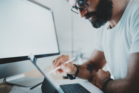 Close up view of bearded man in white tshirt working with portable tablet computer.Designer drawing digital plans at modern lightful office.Horizontal.Blurred background.Cropped.の写真素材