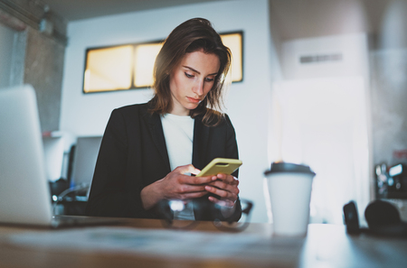 Businesswoman typing text message on smartphone while working at office.Blurred background.の写真素材