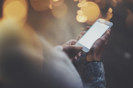 Woman holding hands smartphone in night atmospheric city.Female hands using mobile phone.Closeup on blurred background.Flares, bokeh effects.の写真素材