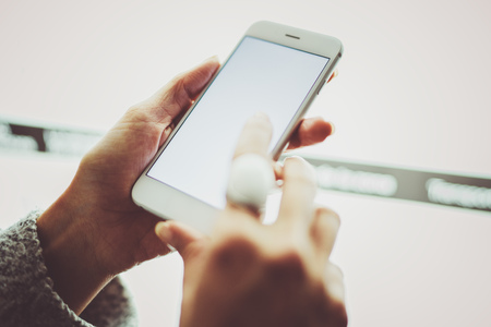 Girl pointing finger on screen smartphone.Female hands texting message mobile phone.Closeup on blurred light coloured background.の写真素材
