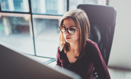 Attractive young businesswoman using desktop computer at modern working place at office.Blurred background.Horizontal.の写真素材