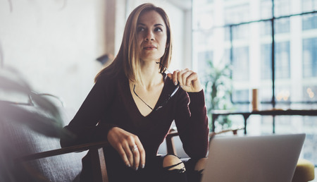 Closeup view of young beautiful woman sitting at the comfortable armchair and using laptop computer.Working process at coworking studio.Horizontal, blurred background.の写真素材