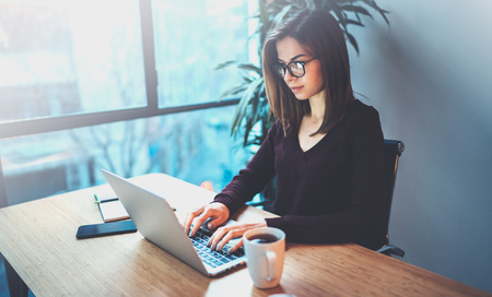 Student girl wearing eye glasses working on laptop at her workplace at night office.Horizontal.Blurred background.Flares.の写真素材