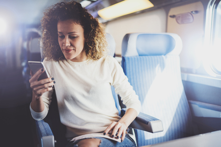 Enjoying travel concept. Young pretty woman tourist traveling by the train sitting near the window using smartphone.の写真素材