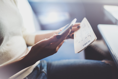 Enjoying business travel concept. Young beautiful brunette tourist girl travelling on the train sitting near the window using smartphone,holding ticket hands.Horizontal closeup.の写真素材
