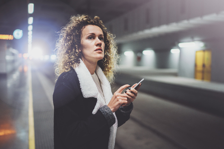 Traveler woman texting a smartphone while is waiting with a suitcase in an airport or a rail train stationの写真素材