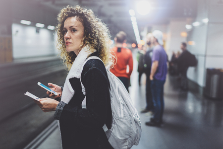 Attractive woman with backpack on transit platform using smartphone for make photo of train ticket while waiting rail train on metro station.の写真素材