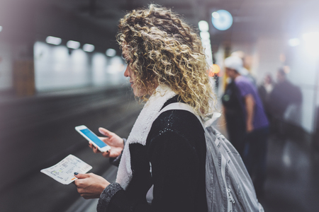 Attractive woman with backpack on transit platform using smartphone for make photo of train ticket while waiting rail train on metro station.の写真素材