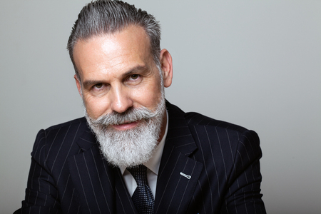 Portrait of attractive middle aged bearded gentleman wearing trendy suit over empty gray background. Studio shot, business fashion concept.の写真素材