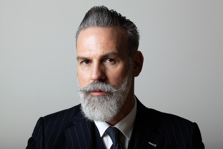 Portrait of elegant middle aged bearded gentleman wearing trendy suit over empty gray background. Studio shot, business fashion concept.の写真素材