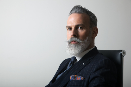 Portrait of confident bearded middle aged gentleman wearing trendy suit over empty gray background. Copy Paste space. Studio shotの写真素材
