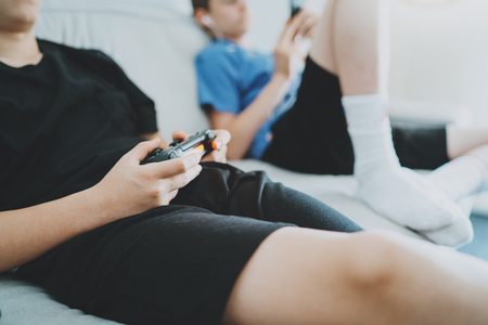Brothers sitting on a sofa in living room and playing video games. Family relaxing time at home concept.の写真素材
