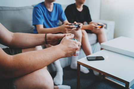 Young teenage sitting on a sofa in living room and playing video games. Family relaxing time at home concept. Closeup.の写真素材