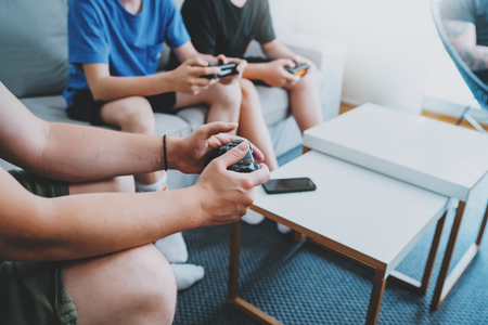 Young friends sitting on a sofa in living room and playing video games. Family relaxing time at home concept.の写真素材