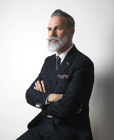 Portrait of attractive bearded middle aged gentleman wearing trendy suit over empty gray background. Studio shot. Verticalの写真素材