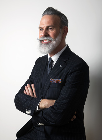 Portrait of positive bearded middle aged gentleman wearing trendy suit over empty gray background. Studio shot. Verticalの写真素材
