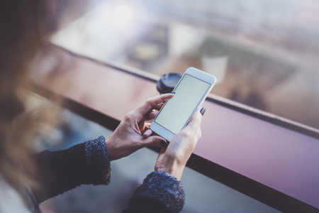 Woman holding hands smartphone and texting message.Female hands using mobile phone.Closeup on blurred background.Flares, bokeh effects. Mock-up.の写真素材
