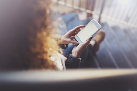 Woman holding hands smartphone and texting message.Female hands using mobile phone.Closeup on blurred background.Flares, bokeh effects. Mock-up.の写真素材
