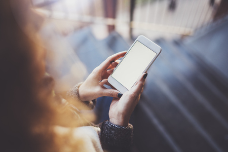 Woman holding hands smartphone and texting message.Female hands using mobile phone.Closeup on blurred background.Flares, bokeh effects. Mock-up.の写真素材