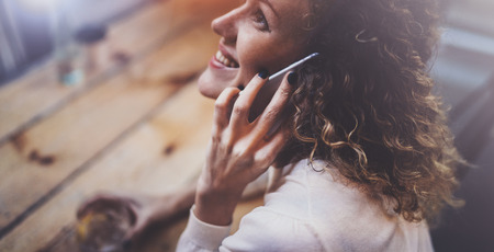 Smiling pretty young woman making conversation call with her friends via cell telephone while sending free time at city cafe. Bokeh and flares effect on blurred background.の写真素材