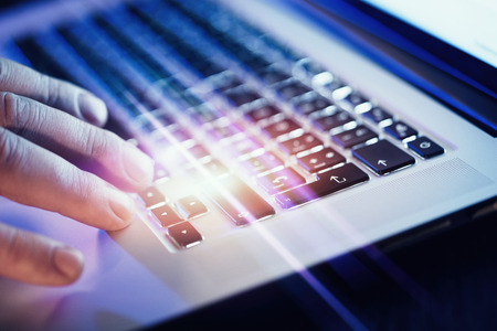 Closeup of male hands typing on laptop keyboard at the office. Visual effects, flares.