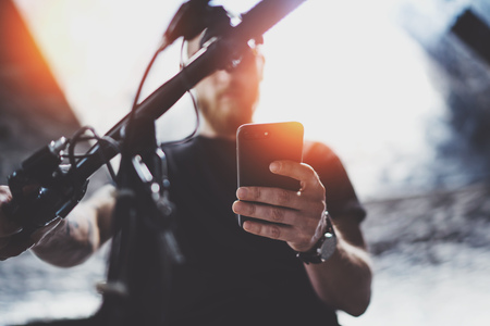 Tattooed muscular male holding mobile phone in hands and using map app for preparing ride road route. Discover urban city by electric scooterの写真素材