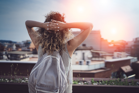 Hansome young woman curly hair and casual wear enjoing beautiful view of the city on sunset.の写真素材