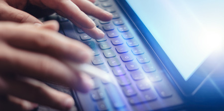 Close-up view of male hands typing on electronic tablet keyboard-dock station. Businessman working at office and using electronic pen and device.の写真素材