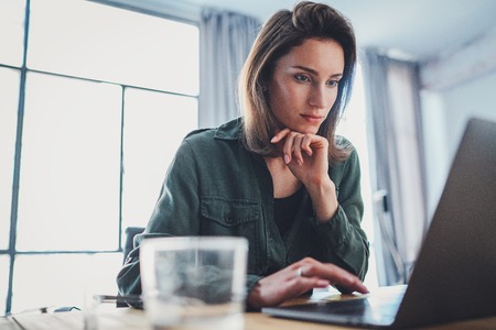 Young beautiful female model sitting at the comfortable armchair and using laptop computer.Working...