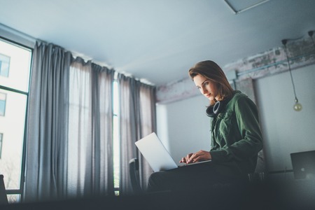 Handsome female coworker sitting at the table and using laptop computer.Working process at coworking studio.Panoramic windows on blurred background.の写真素材