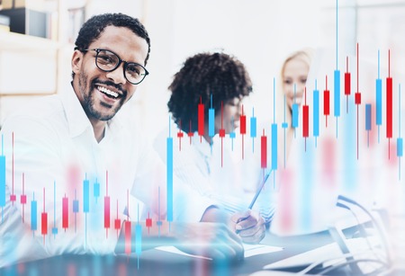 Teamwork traiding concept.African american man in white shirt smiling at the camera. Red and green candlestick chart and stock trading computer screen background. Double exposure.の写真素材