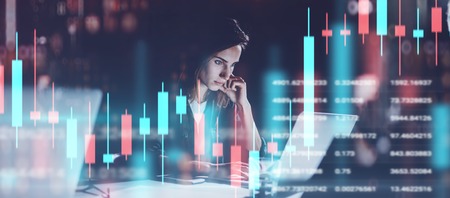 Young woman working at night modern office.Technical price graph and indicator, red and green candlestick chart and stock trading computer screen background. Double exposure.Wide.の写真素材