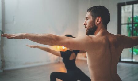 Young sportive man and woman are practicing yoga exercises in the studio. Couple of young sporty people practicing yoga lesson with partnerの写真素材