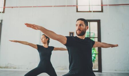 Young sportive man and woman are practicing yoga exercises in the studio. Couple of young sporty people practicing yoga lesson with partnerの写真素材